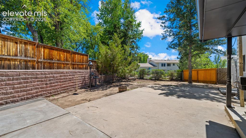 Image 32 of 44: Expansive concrete patio with block retaining wall and wood fencing