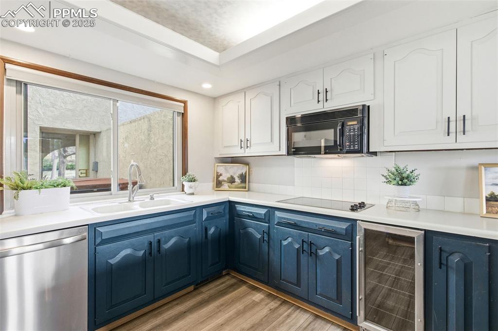 Image 14 of 45: Kitchen featuring beverage cooler, black appliances, white cabinets, blue c