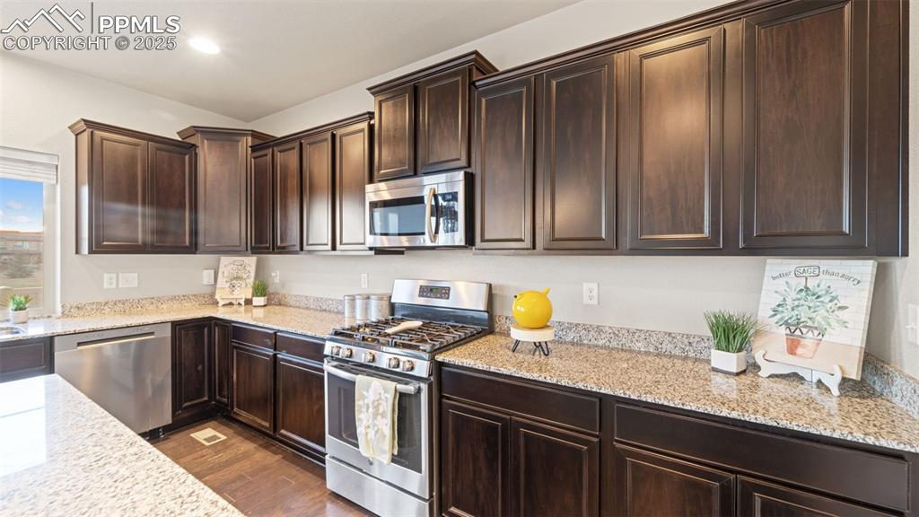 Image 13 of 48: Kitchen with stainless steel appliances, dark brown cabinets, light stone c