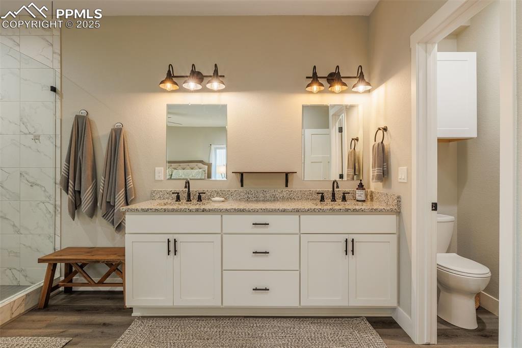 Image 22 of 38: bathroom featuring wood finished floors, double vanity, and a tile shower