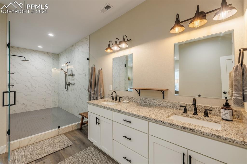 Image 23 of 38: Full bathroom with wood finished floors, a tile shower, double vanity, and 