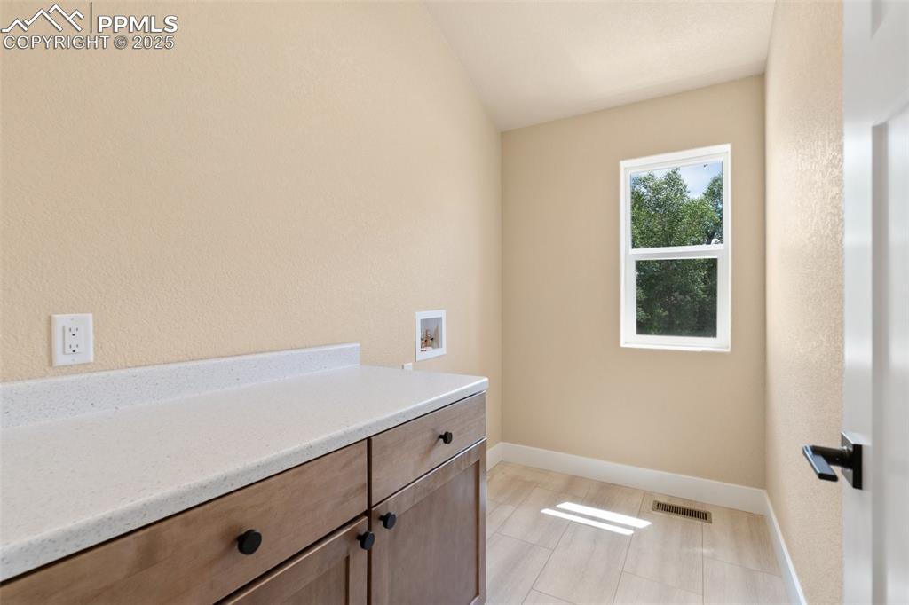 Image 28 of 33: Upper level full laundry room with counter, cabinets/storage, and window
