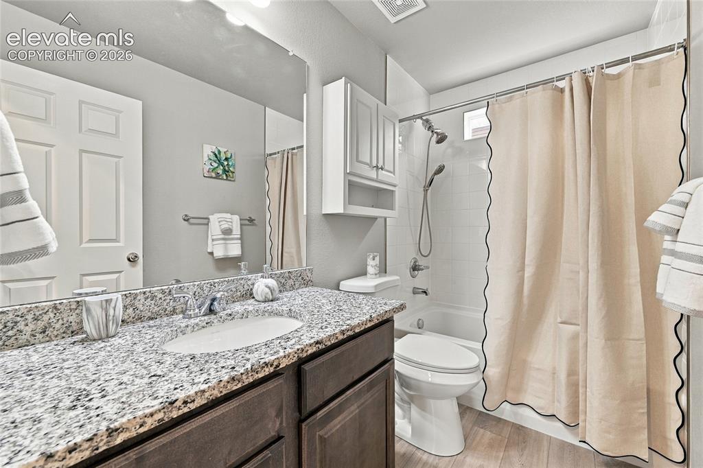 Image 13 of 30: Granite countertop vanity with integrated sink, wood-finish cabinetry, and