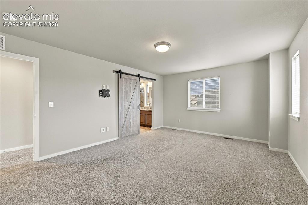 Image 20 of 30: Carpeted interior with light gray walls, multiple windows, and a barn door