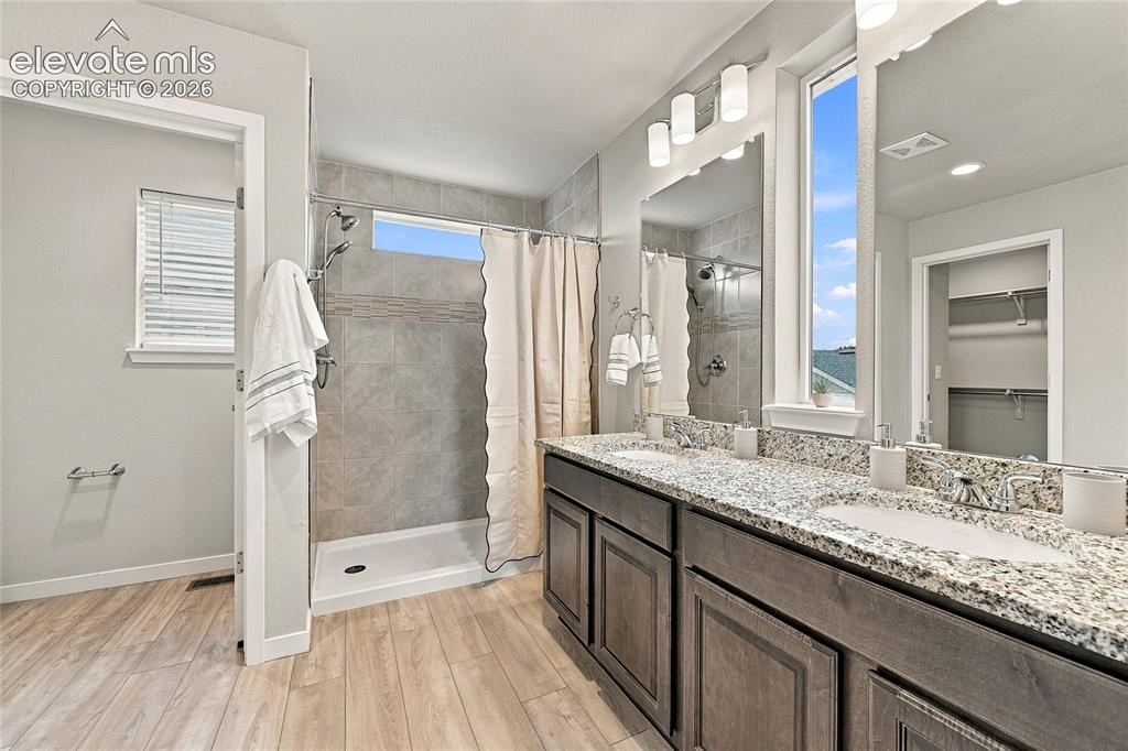 Image 21 of 30: Dual vanities with stone-finish countertops, wood-finish flooring, tiled sh