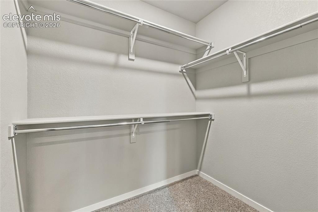 Image 23 of 30: Walk-in closet with white shelving, chrome hanging rods, and light-colored 