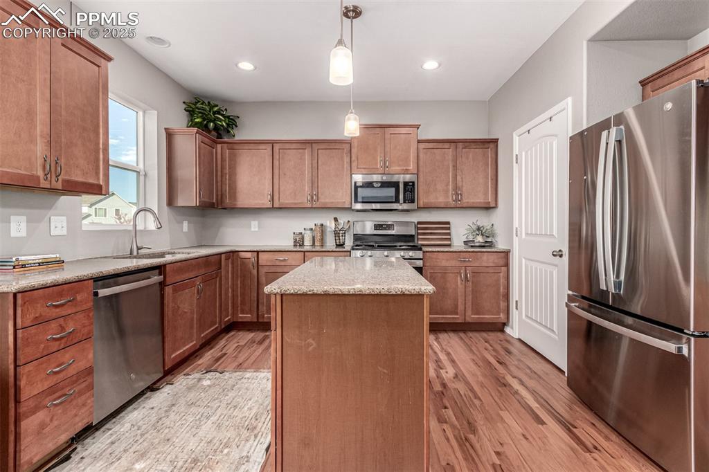 Image 12 of 41: Kitchen with stainless steel appliances, brown cabinetry, decorative light 