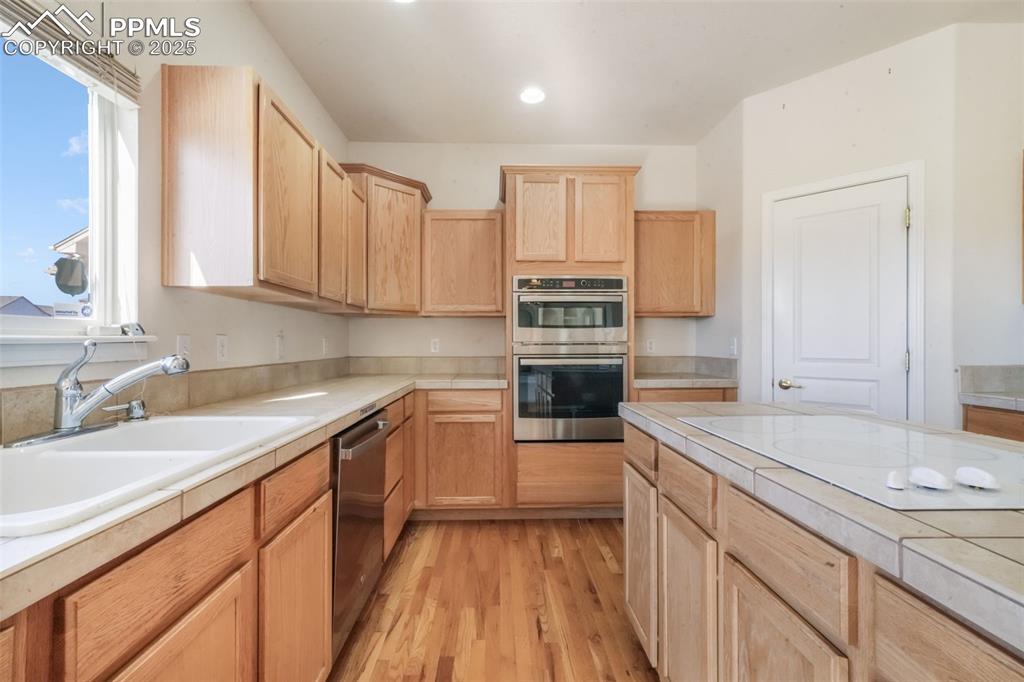 Image 6 of 50: Kitchen with tile countertops, light brown cabinetry, stainless steel appli