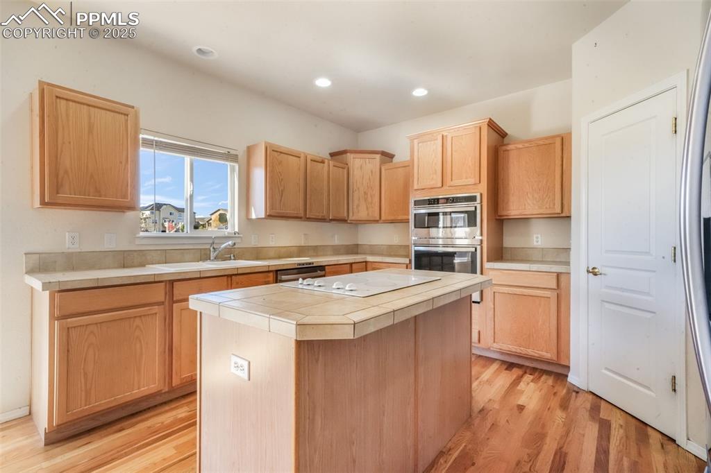 Image 7 of 50: Kitchen featuring tile countertops, a center island, light wood-style floor