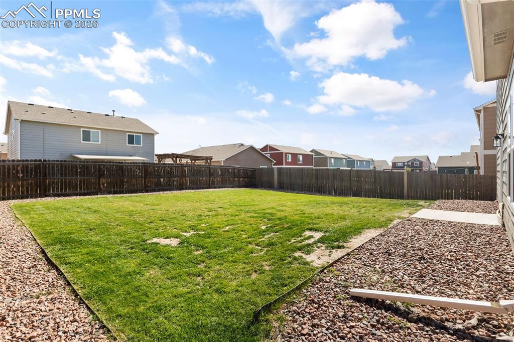 Image 24 of 25: Expansive fenced backyard featuring a grassy lawn, gravel landscaping, and 