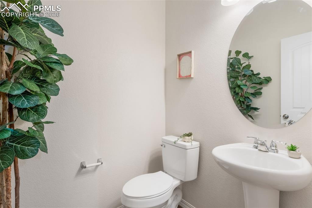 Image 7 of 25: Pedestal sink with chrome faucet, circular wall mirror, and neutral wall pa