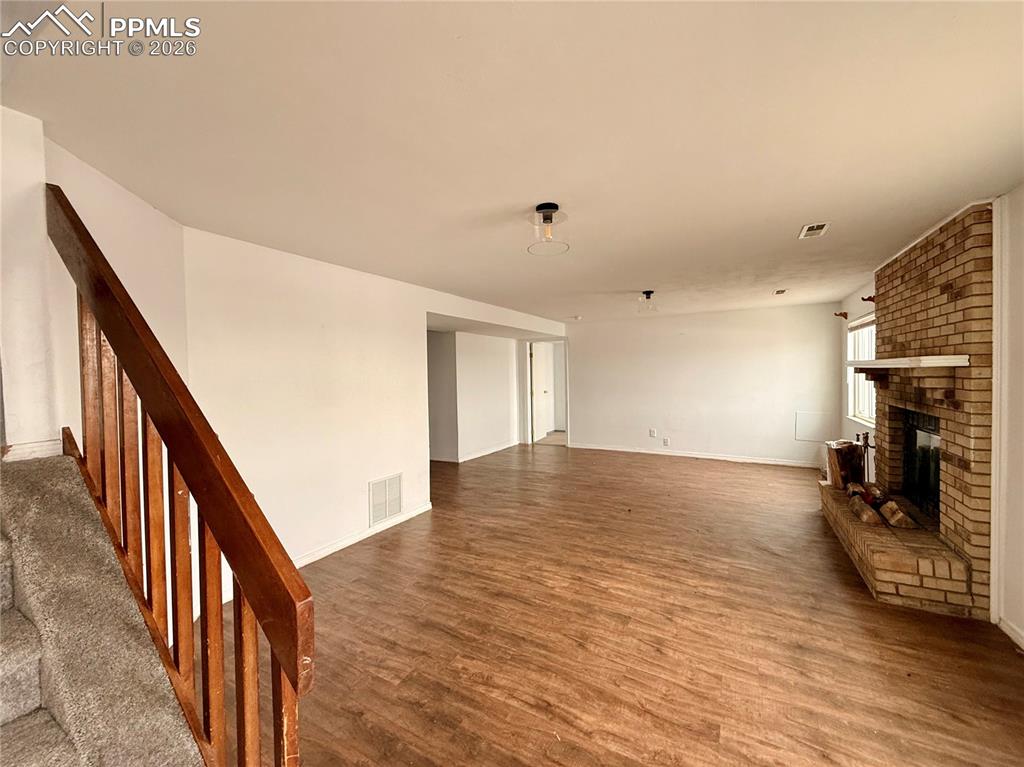 Image 24 of 42: Unfurnished living room with a brick fireplace, wood finished floors, and s