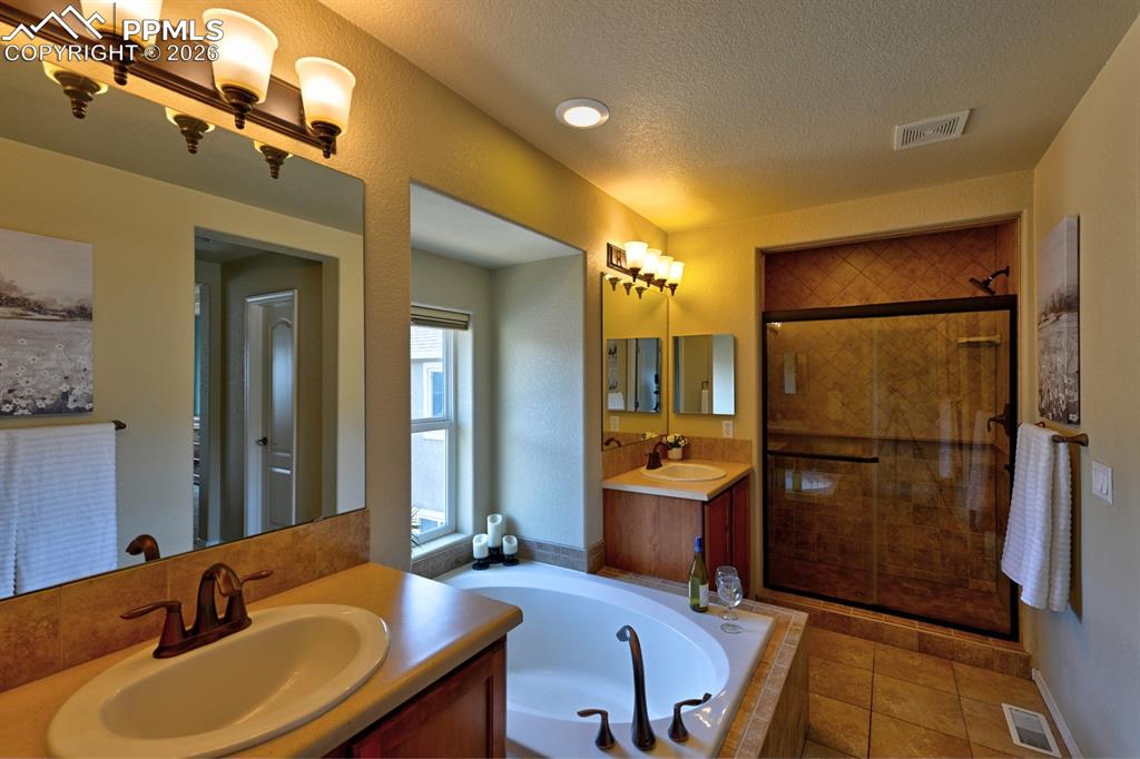 Image 15 of 33: Primary bath with dual vanities, soaking tub, and walk in shower with tile 