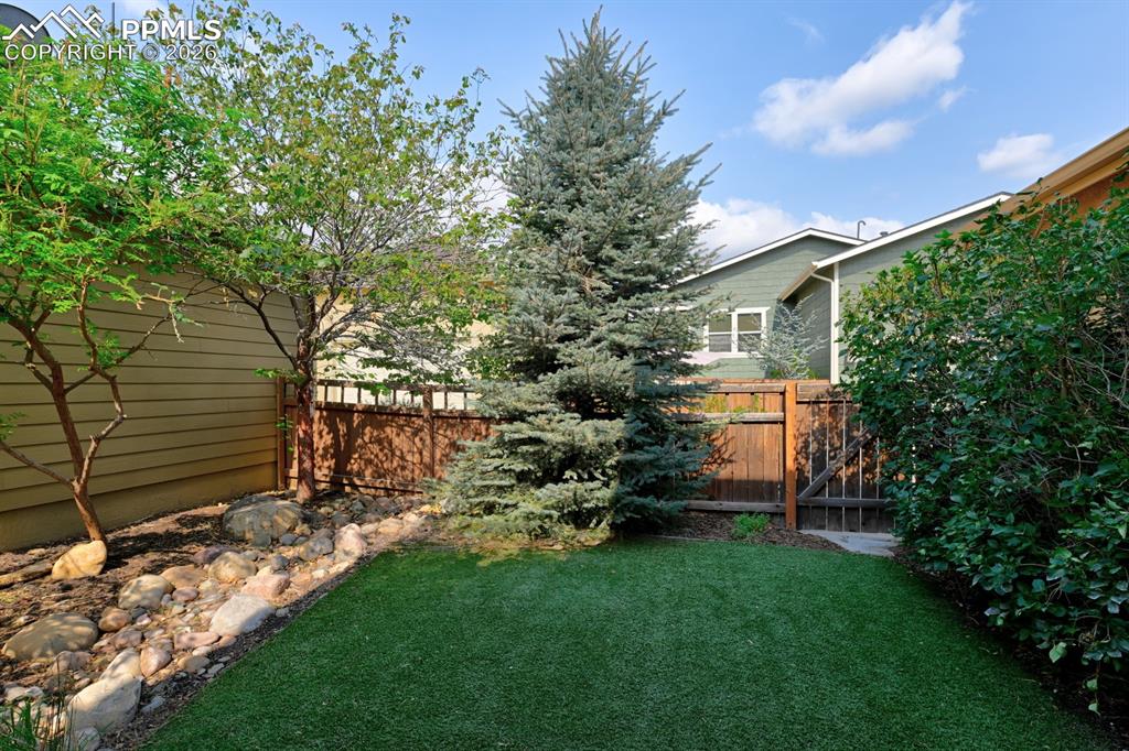 Image 19 of 33: Beautifully landscaped turf yard with mature trees and fencing offers low m