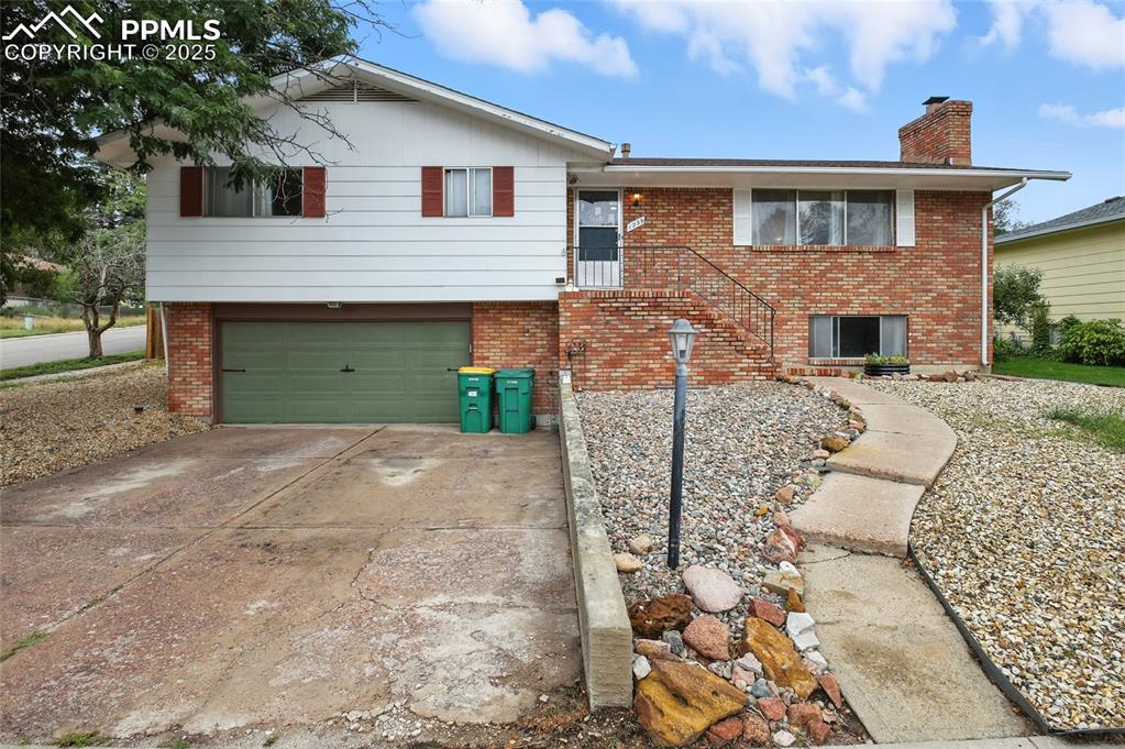 Caption: View of front of property with brick siding, concrete driveway, a chimney, and an attached garage