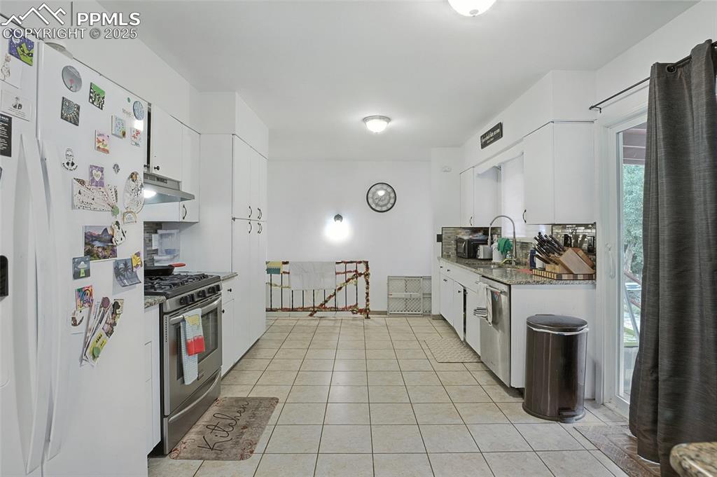 Image 13 of 35: Kitchen with appliances with stainless steel finishes, white cabinetry, lig
