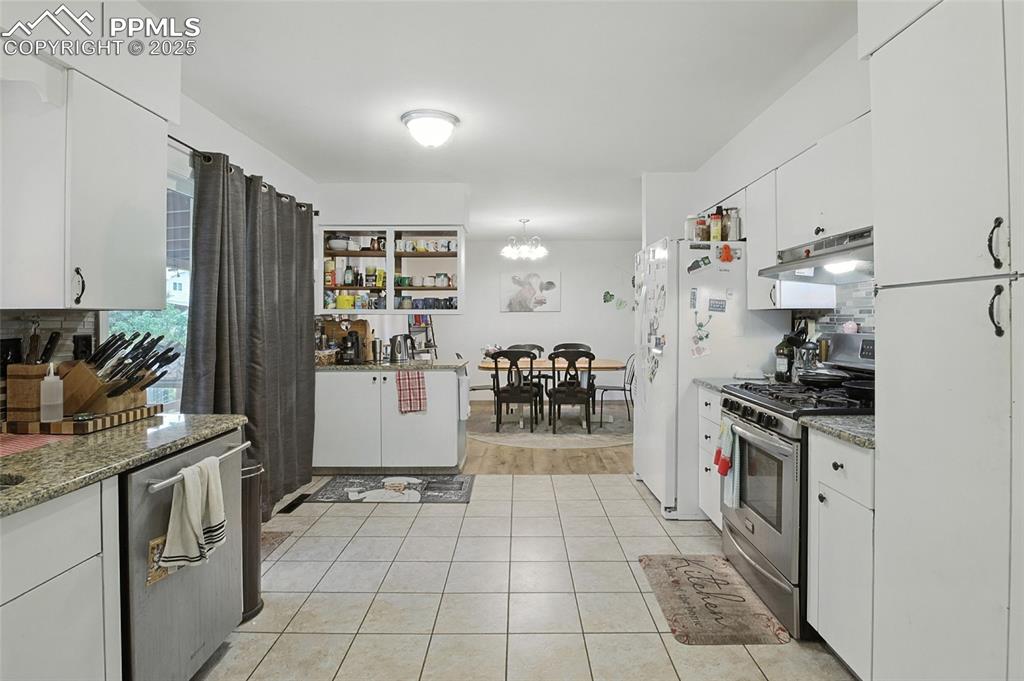 Image 14 of 35: Kitchen with white cabinetry, stainless steel range with gas stovetop, ligh