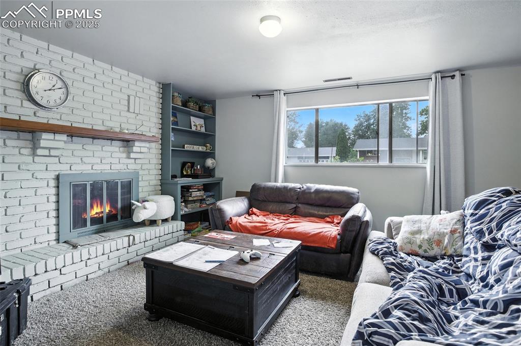 Image 24 of 35: Living room with carpet floors and a brick fireplace