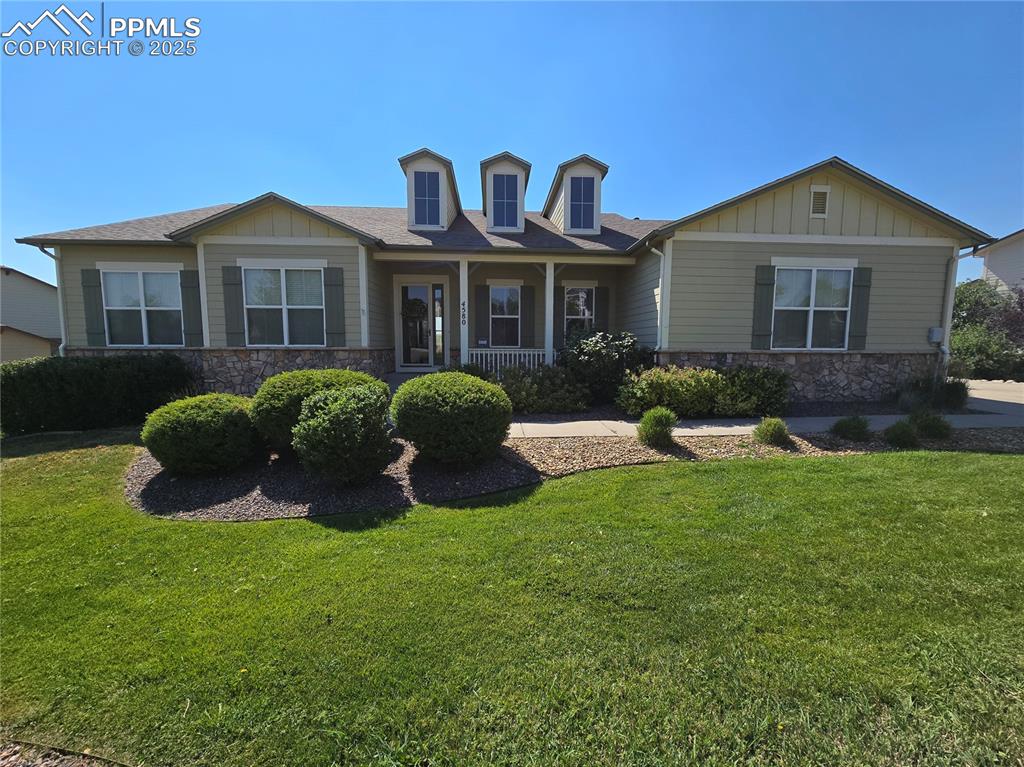 Caption: View of front of house with stone siding, covered porch, and a front lawn