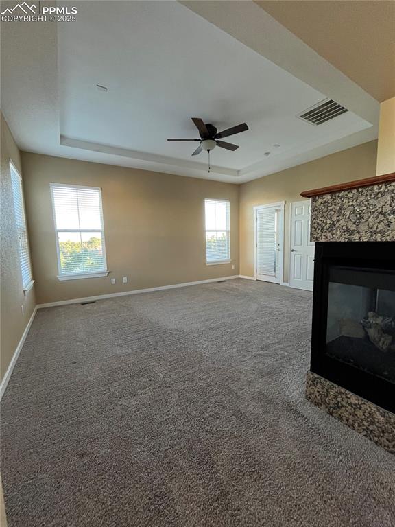 Image 10 of 27: Unfurnished living room with a raised ceiling, carpet, a stone fireplace, a