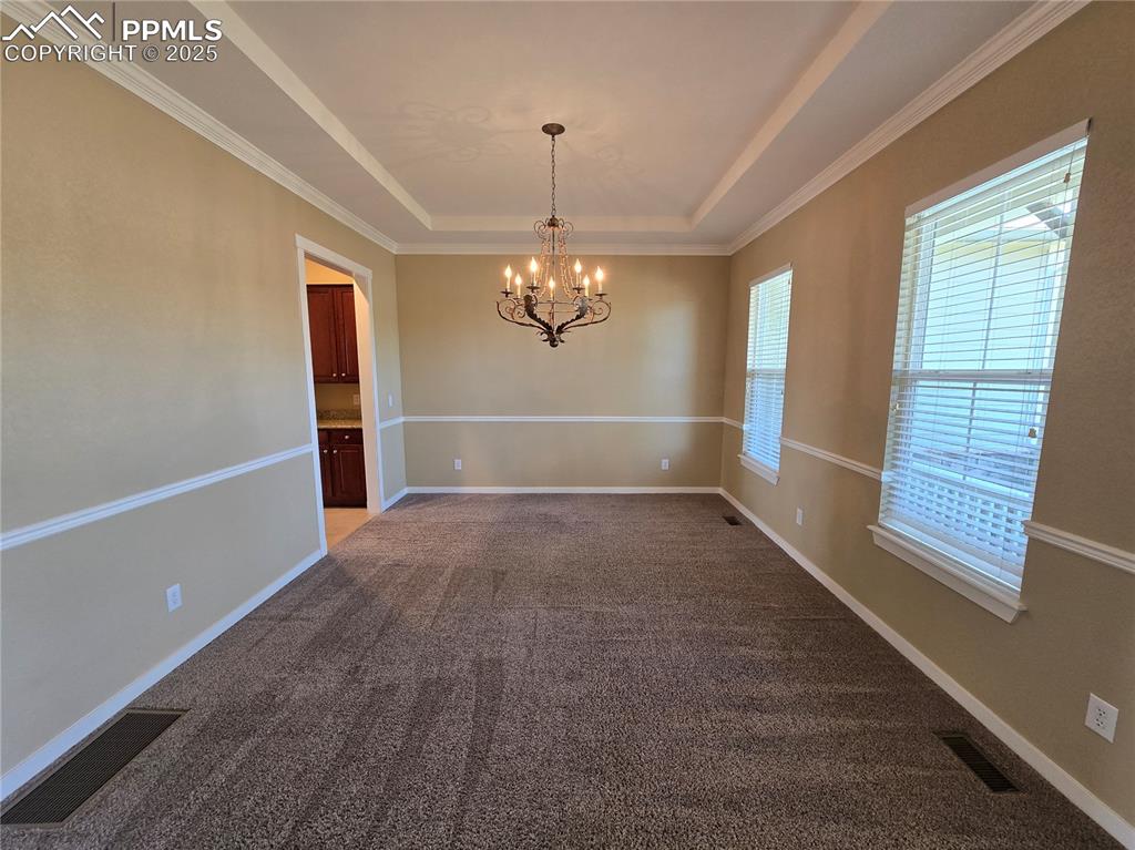 Image 5 of 27: Unfurnished dining area with a raised ceiling, dark colored carpet, ornamen