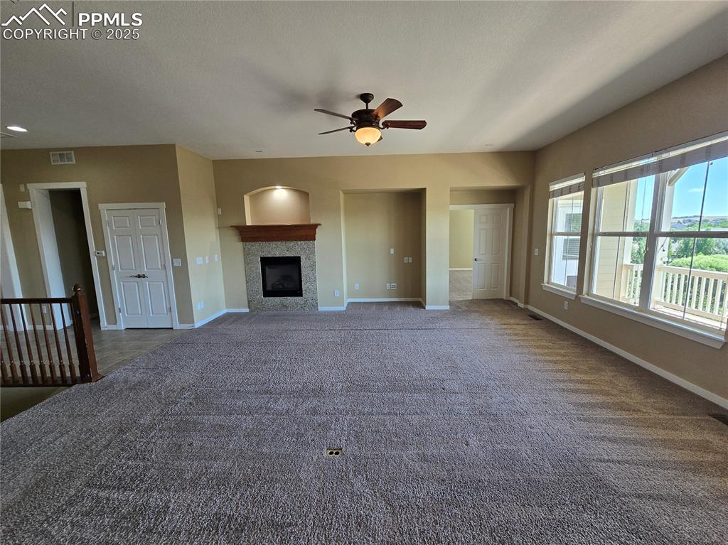 Image 6 of 27: Unfurnished living room with a fireplace, a ceiling fan, and dark carpet