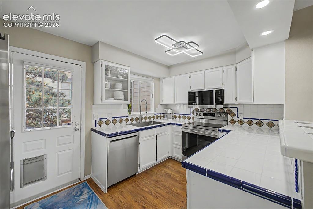 Image 15 of 42: Kitchen featuring white cabinetry, tile countertops with a blue trim, and s
