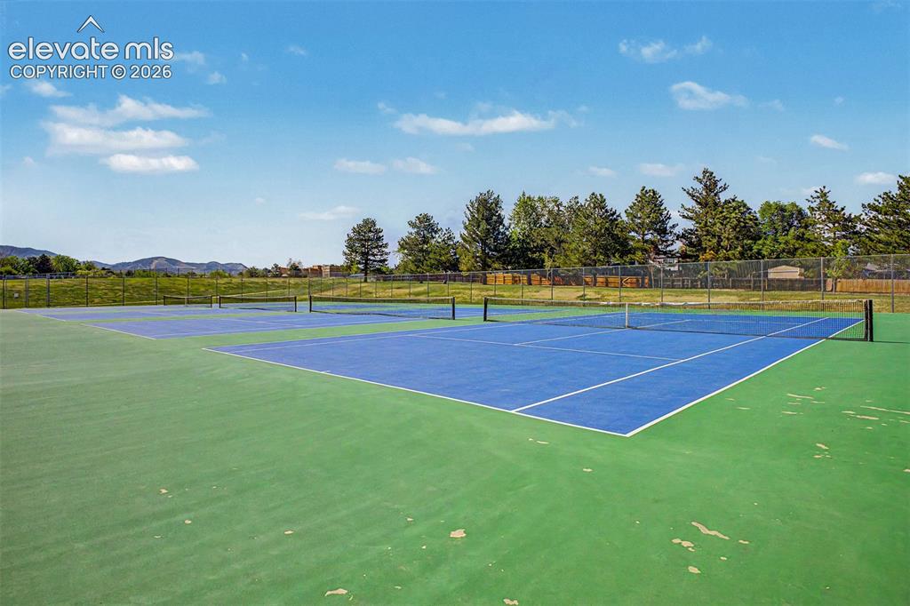 Image 40 of 42: Multiple tennis courts with blue playing surfaces and green surrounds, encl