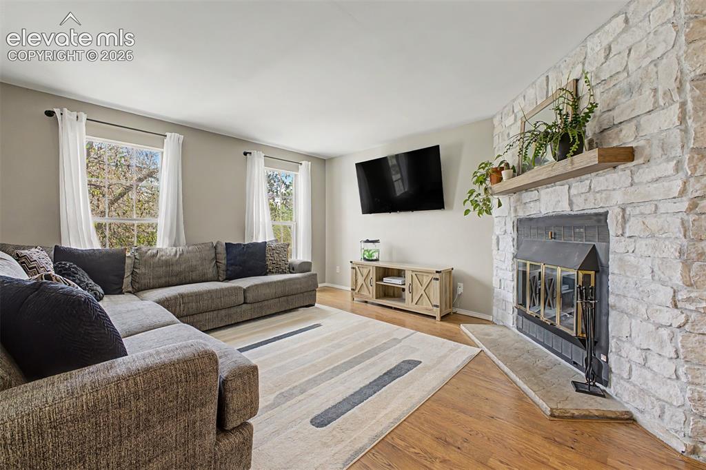 Image 9 of 42: Living area featuring a stone-clad fireplace with a wood mantel, ample natu