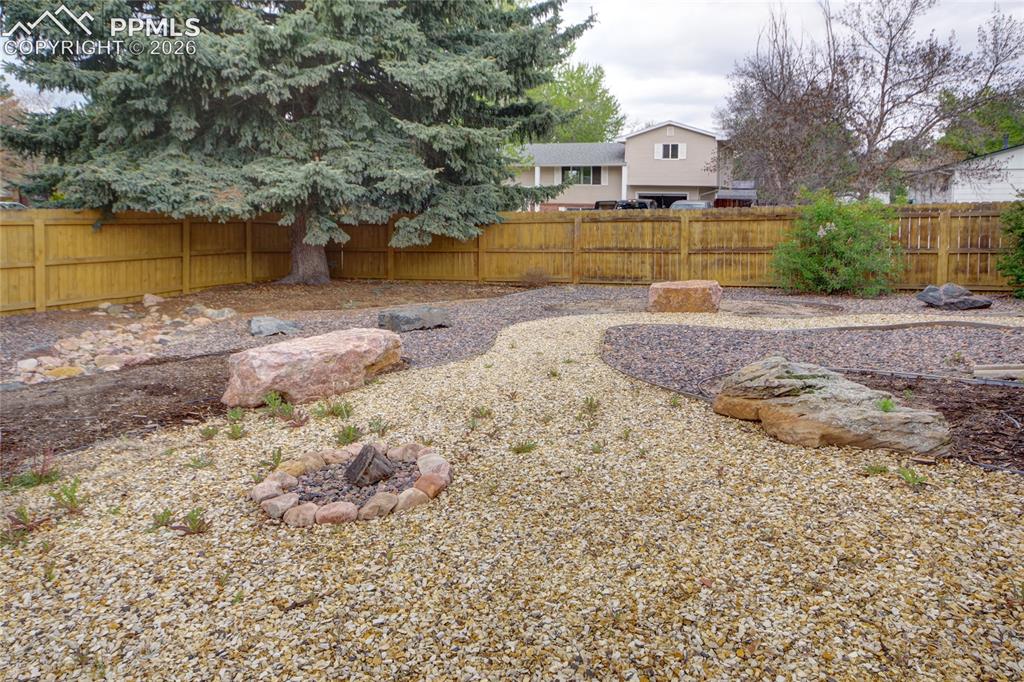 Image 32 of 33: Landscaped outdoor area featuring a rock-lined fire pit, a perimeter wood f