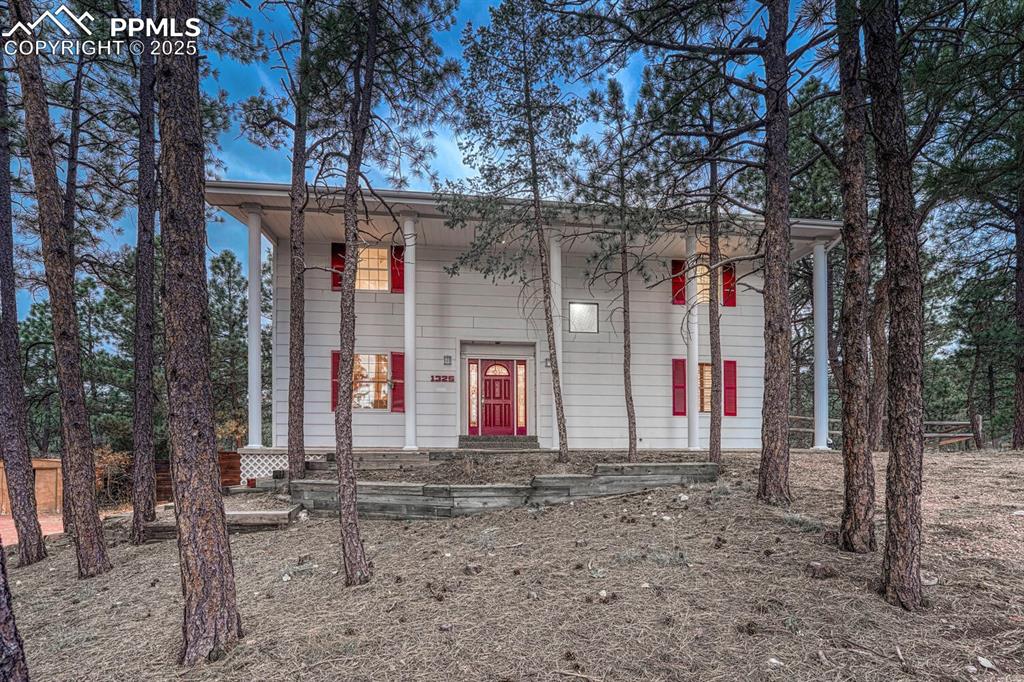 Image 5 of 50: Front of home with terraced planter beds and mature trees.