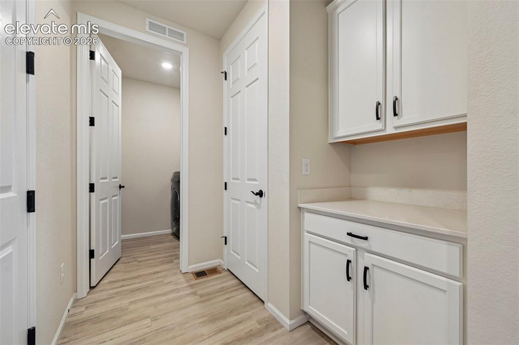 Image 13 of 31: Wood-finish flooring, white cabinetry with black hardware, and a solid surf