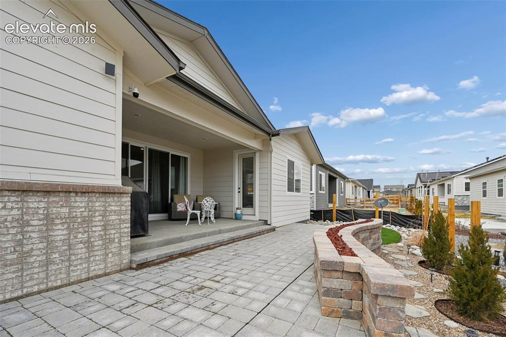Image 31 of 31: Covered patio featuring a sliding glass door, brick facade, and paver stone