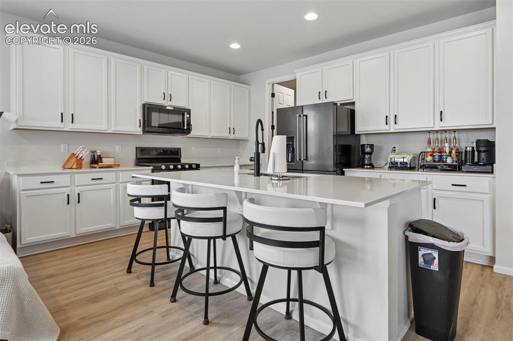Image 6 of 31: Expansive kitchen featuring white cabinetry, light-toned countertops, a cen
