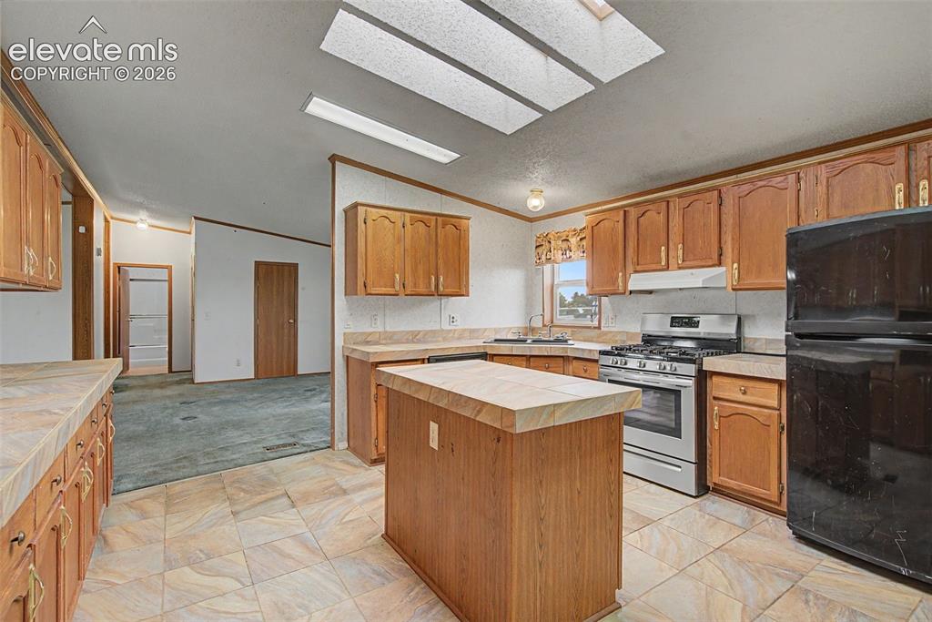 Image 10 of 26: Kitchen featuring tile flooring, wooden cabinetry, and a central island wit