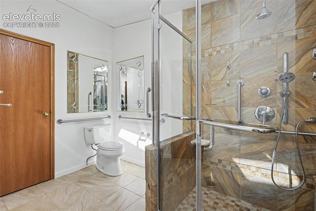 Image 15 of 26: Spacious shower stall with stone-look wall tile, glass enclosure, and multi