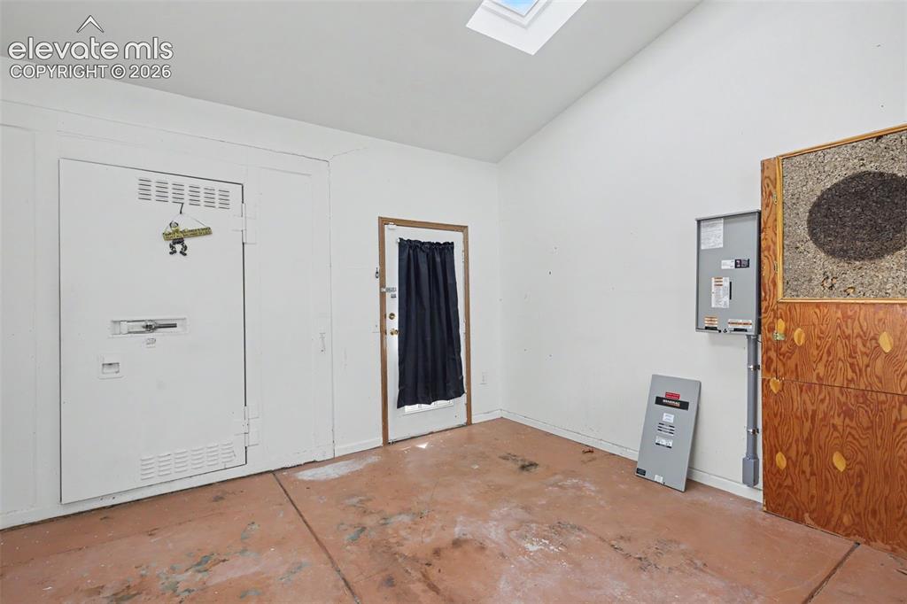 Image 20 of 26: White interior space featuring a skylight, vaulted ceiling, and an exterior