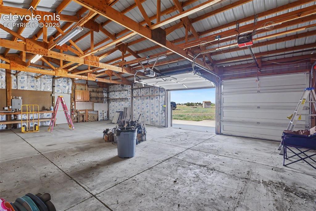 Image 25 of 26: Spacious garage featuring exposed wood trusses, a corrugated metal ceiling,