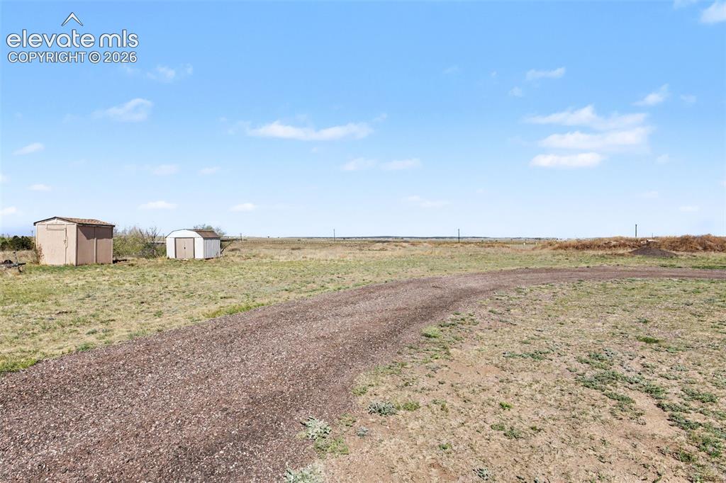 Image 3 of 26: Expansive open land featuring a gravel driveway and two storage sheds