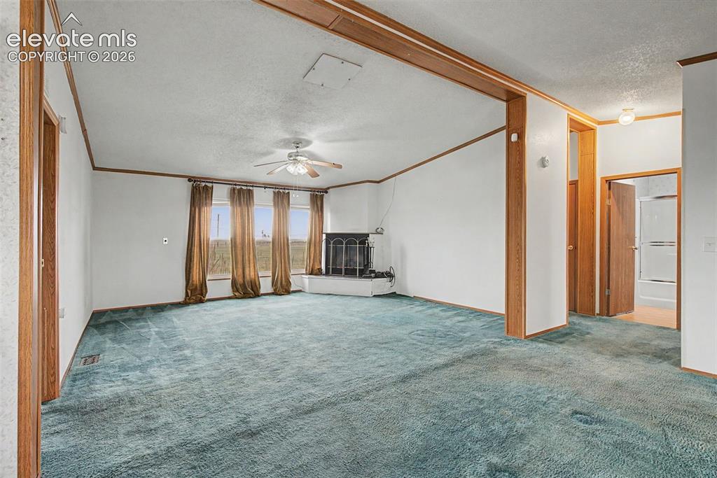 Image 6 of 26: Spacious living room featuring teal carpeting, three large windows, a corne