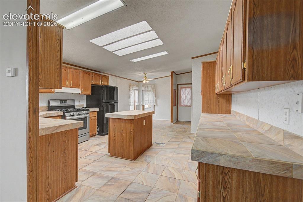 Image 8 of 26: Kitchen featuring wood-finish cabinetry, tile countertops, stainless steel 