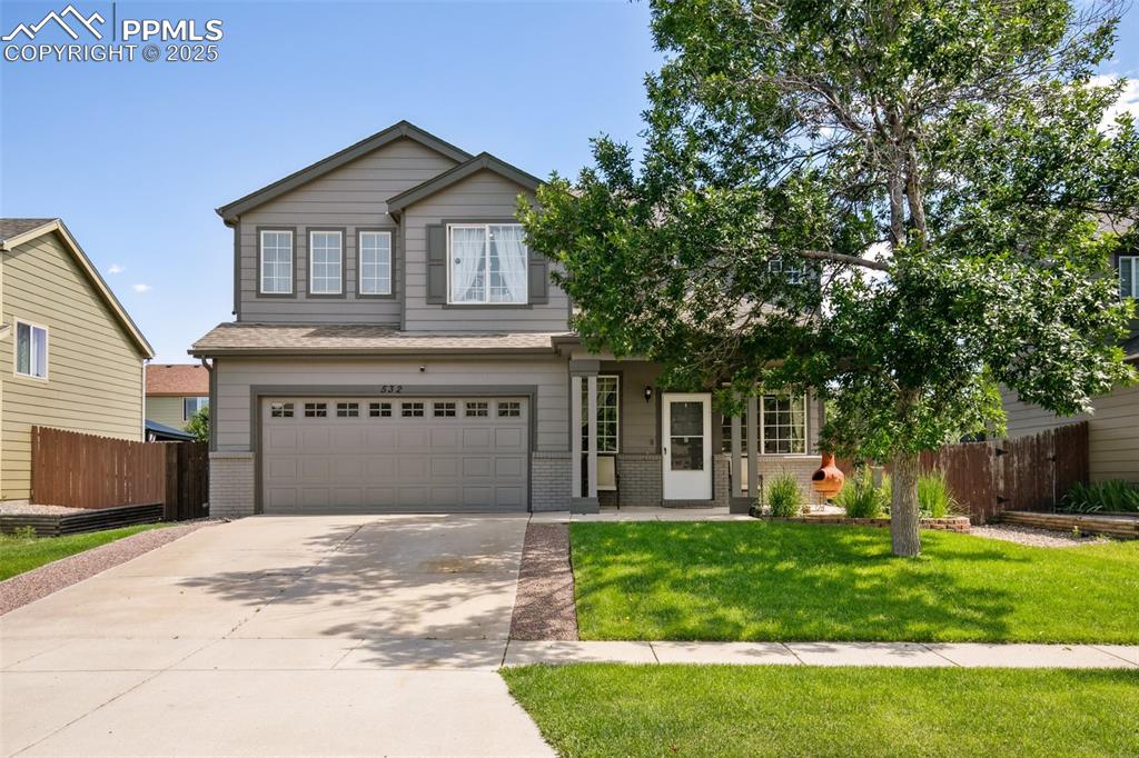 Caption: View of front of house with brick siding, a garage, and concrete driveway