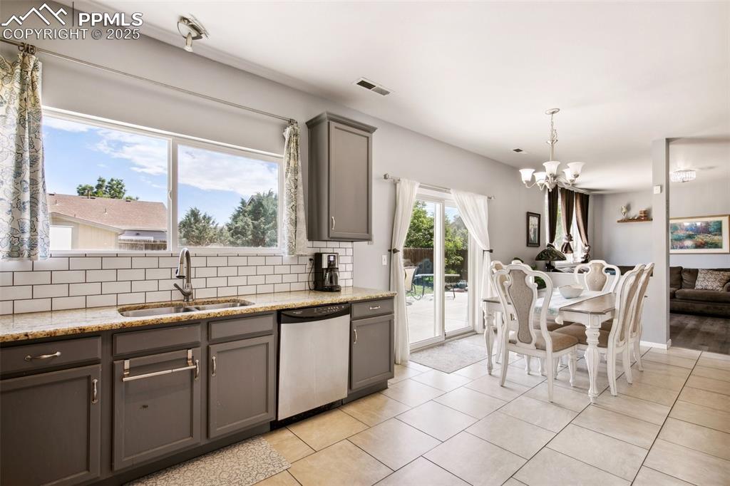 Image 12 of 28: Kitchen with dishwasher, gray cabinets, a chandelier, backsplash, and light