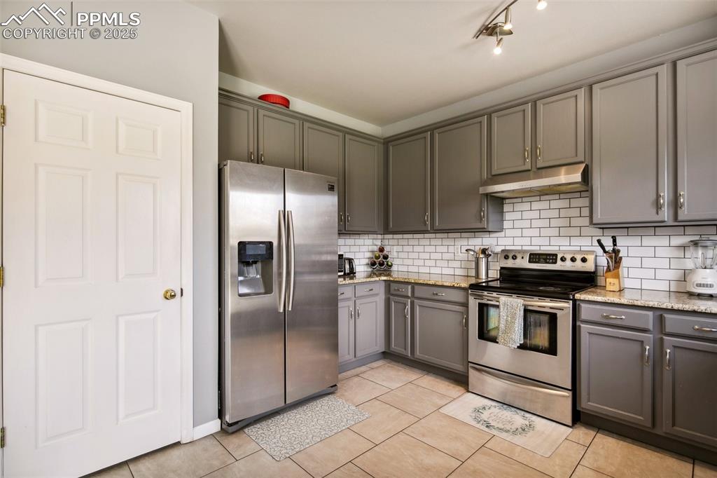 Image 13 of 28: Kitchen with stainless steel appliances, under cabinet range hood, backspla