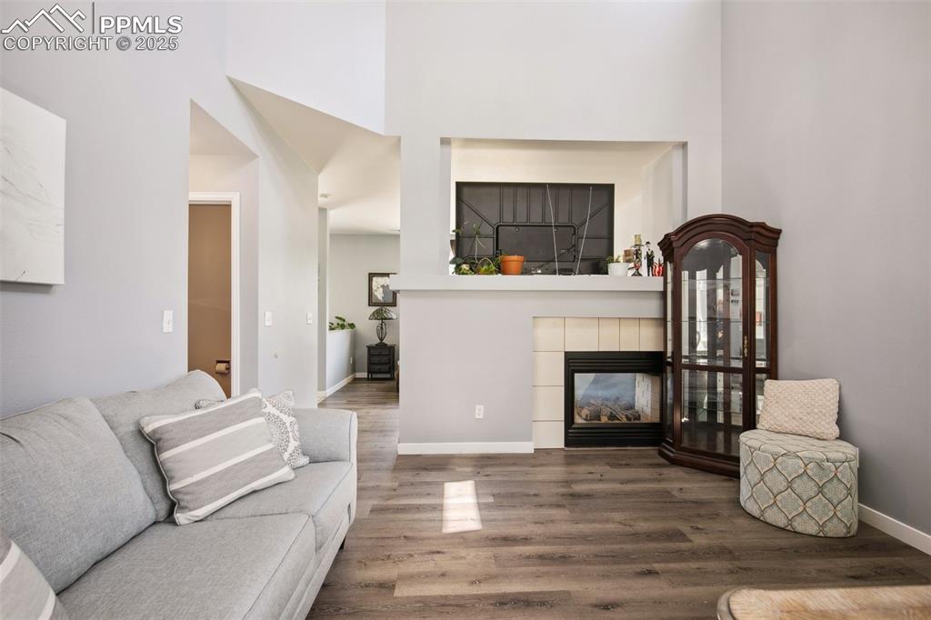 Image 4 of 28: Living area featuring wood finished floors, a high ceiling, and a fireplace