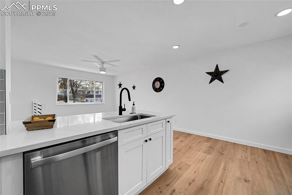 Image 10 of 29: Kitchen with stainless steel dishwasher, white cabinets, light wood-style f