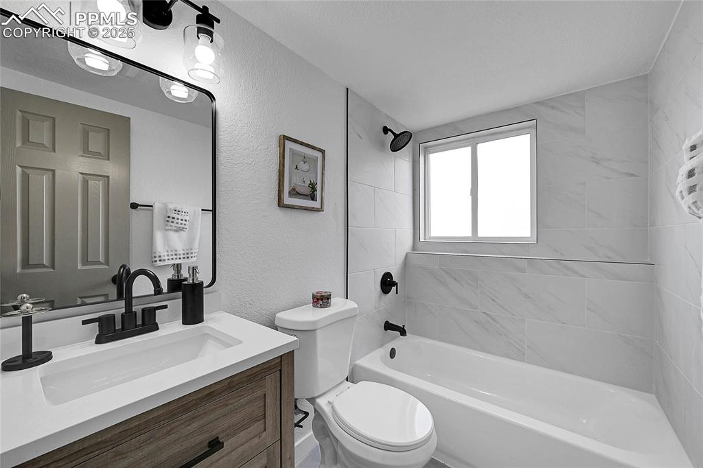 Image 16 of 29: Full bath featuring a textured wall, vanity, and shower / bathtub combinati