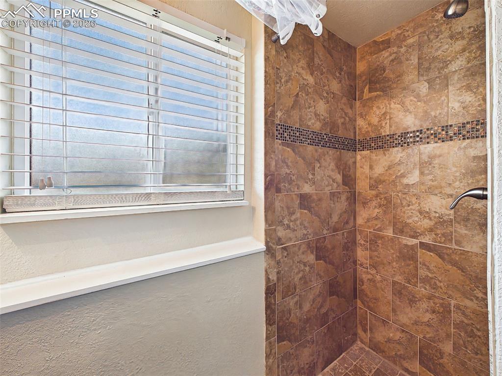 Image 25 of 50: Tiled shower surround featuring decorative accent banding and a nearby wind