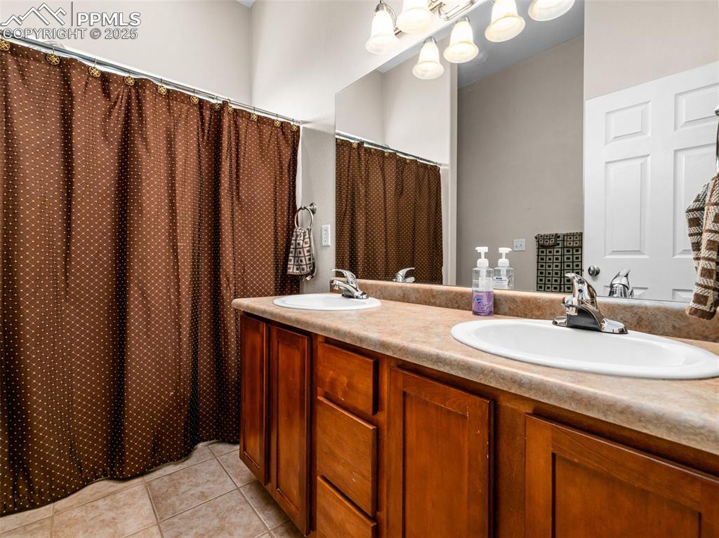Image 12 of 46: Full bathroom with light tile patterned floors, double vanity, and a shower