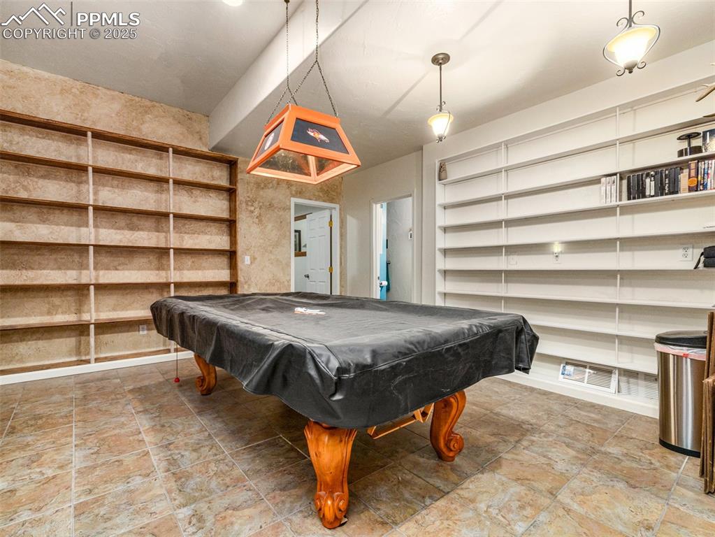 Image 22 of 46: Recreation room with pool table, built in shelves, and light stone finish f